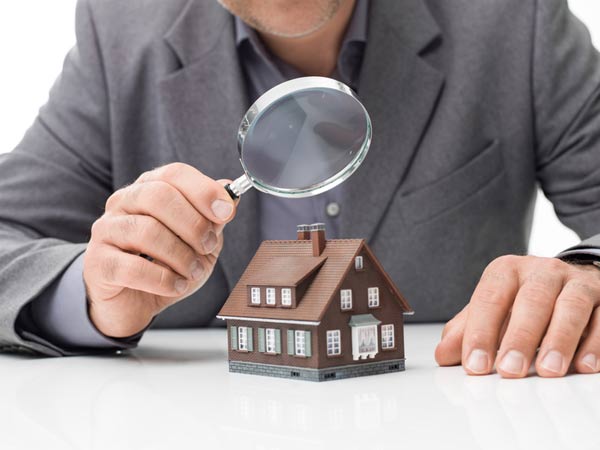 man in suit holding magnifying glass over model home