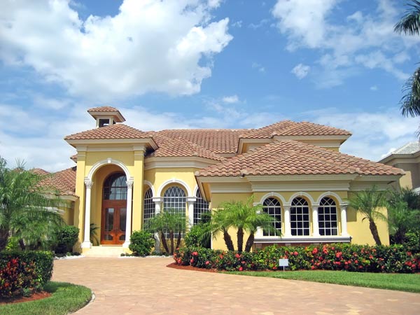 yellow house with brick driveway and palm trees